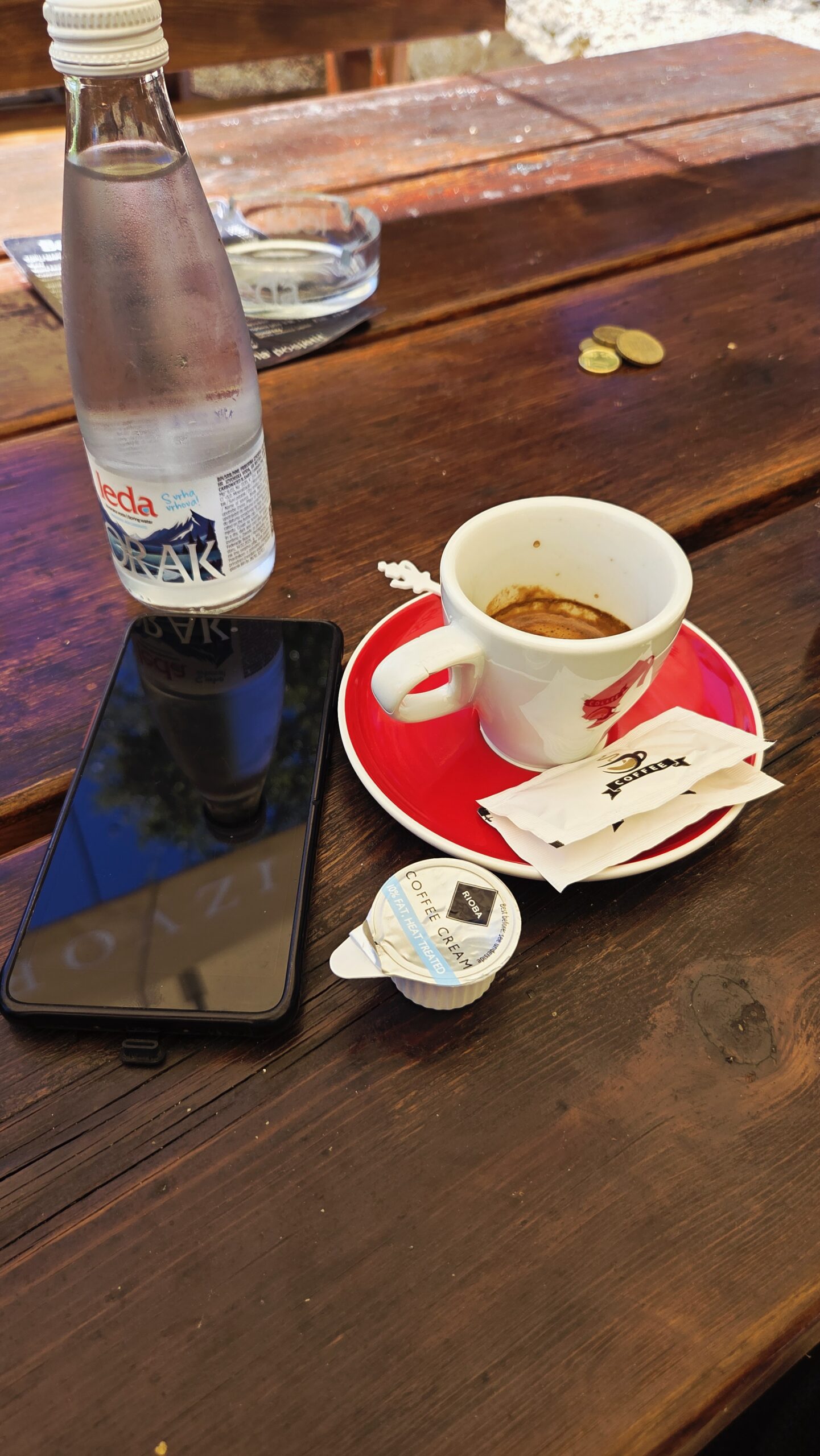 A small espresso on a red saucer with a sugar packet and a milk capsule, on a wooden table