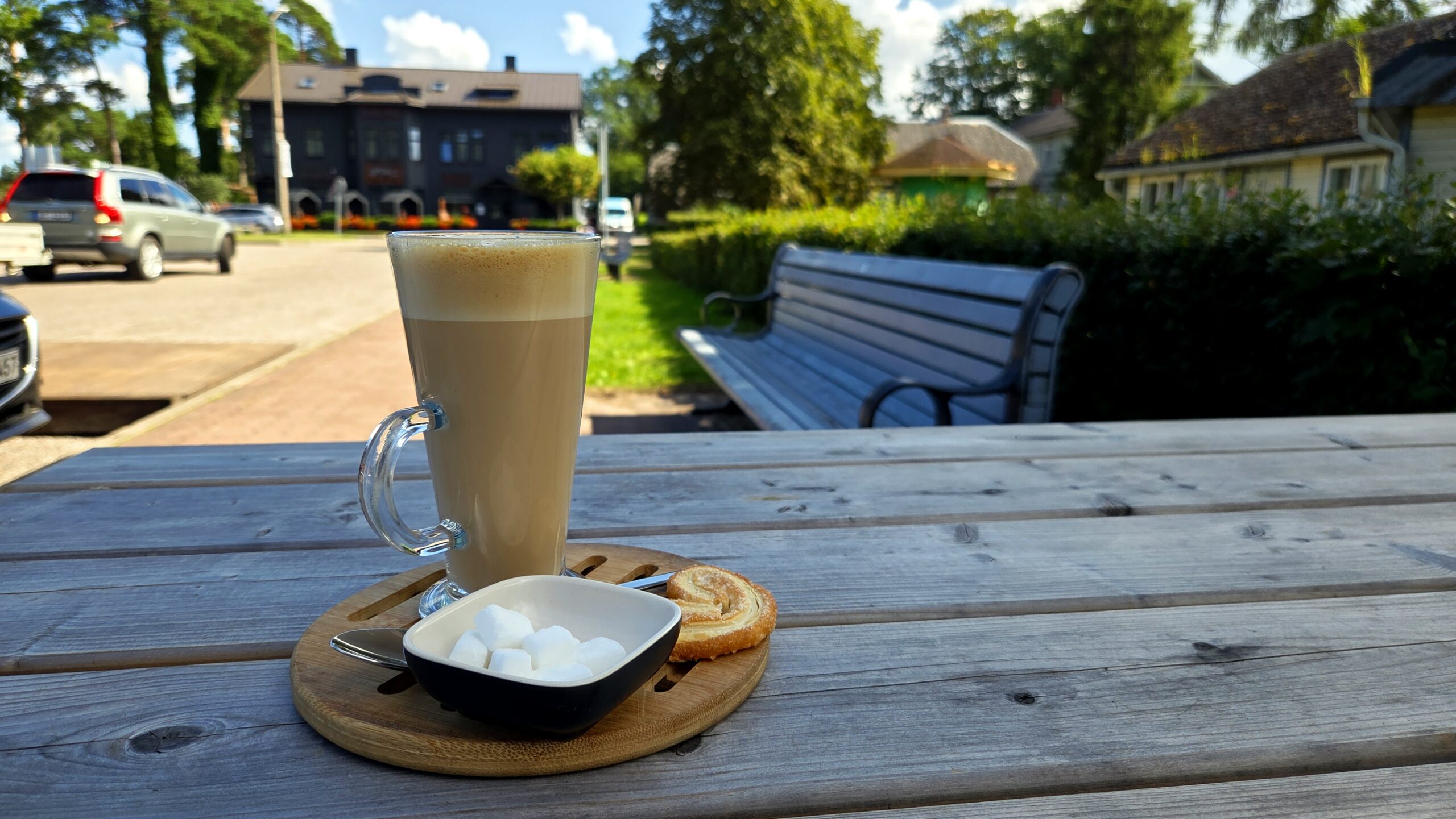 A tall glass of latte with sugar cubes and a cookie on a wooden outdoor table